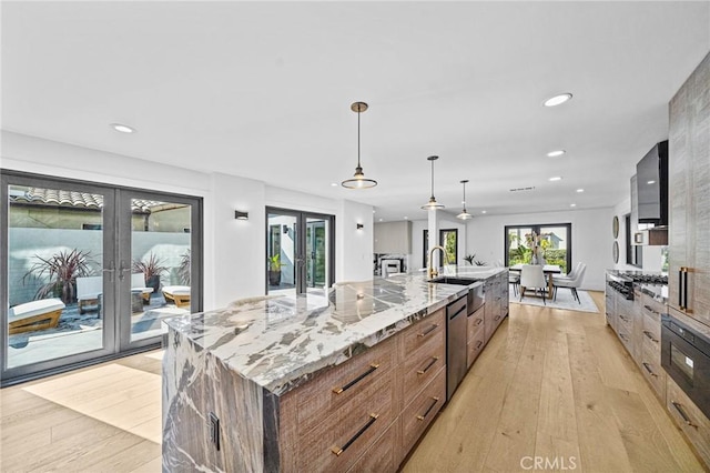 kitchen featuring a large island with sink, light hardwood / wood-style flooring, hanging light fixtures, light stone countertops, and french doors