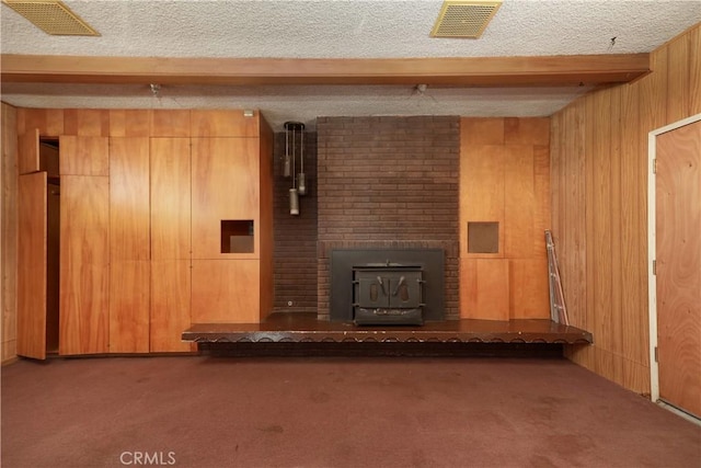 unfurnished living room with visible vents, carpet, beamed ceiling, wood walls, and a textured ceiling