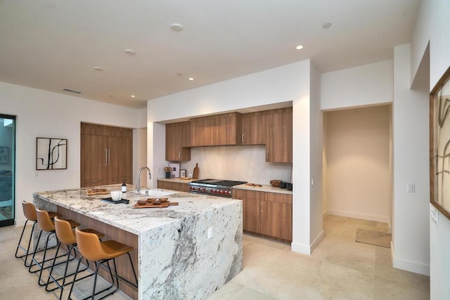 kitchen with light stone countertops, high end stainless steel range oven, a breakfast bar, decorative backsplash, and sink