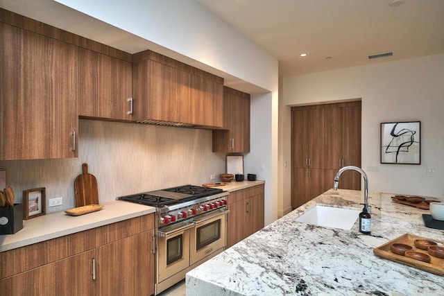 kitchen with cooktop, range with two ovens, light stone counters, decorative backsplash, and sink