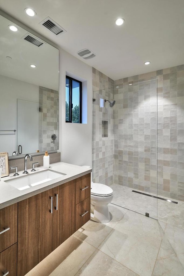 bathroom featuring toilet, a tile shower, and vanity