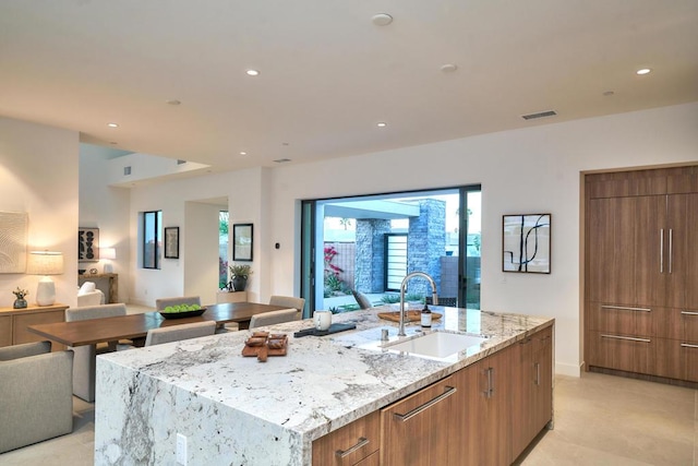 kitchen featuring sink, a kitchen island with sink, and light stone counters