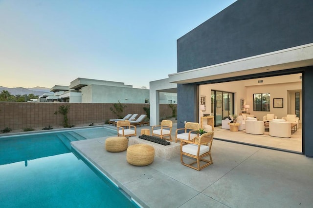 pool at dusk with an outdoor living space with a fire pit, a patio, and a mountain view