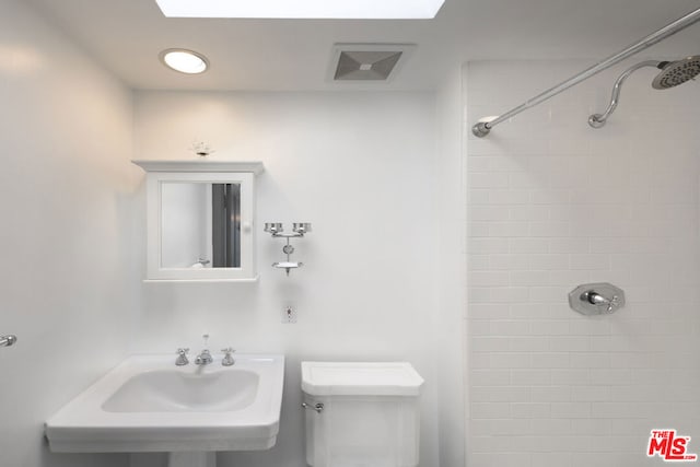 bathroom with toilet, tiled shower, and sink