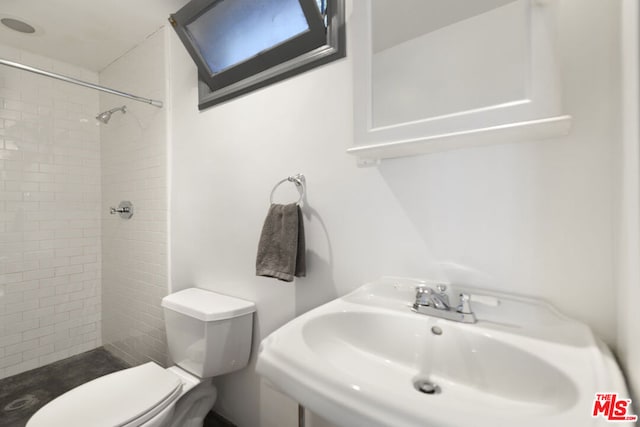 bathroom with sink, a tile shower, and toilet