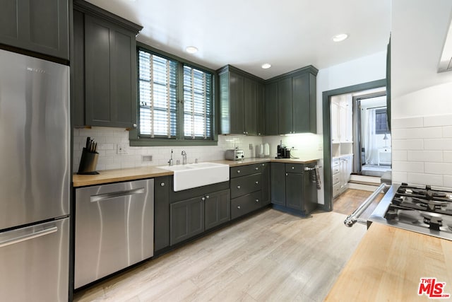 kitchen with butcher block counters, sink, light hardwood / wood-style floors, decorative backsplash, and appliances with stainless steel finishes