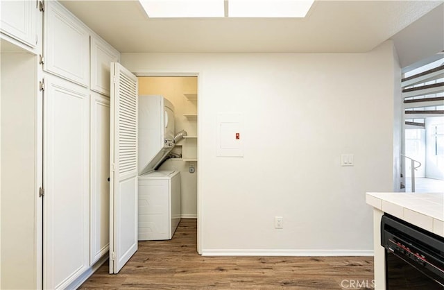 clothes washing area featuring stacked washing maching and dryer, light wood-type flooring, and electric panel