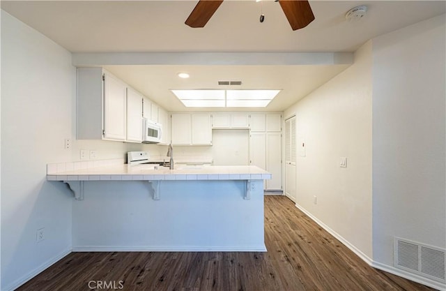 kitchen with white appliances, dark hardwood / wood-style flooring, white cabinetry, and kitchen peninsula