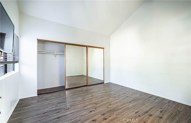 unfurnished bedroom with lofted ceiling, a closet, and dark wood-type flooring