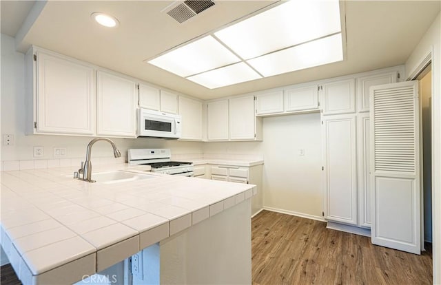 kitchen featuring white appliances, kitchen peninsula, tile countertops, white cabinetry, and sink