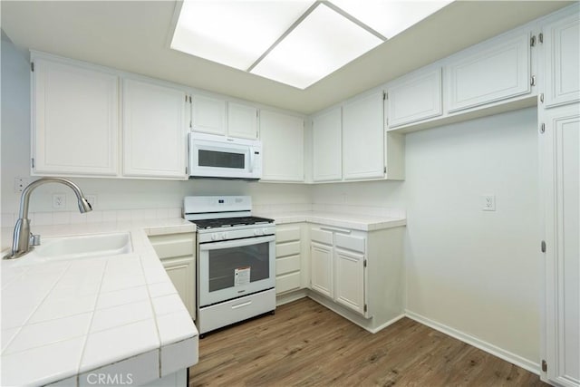 kitchen with white appliances, hardwood / wood-style floors, tile countertops, white cabinets, and sink