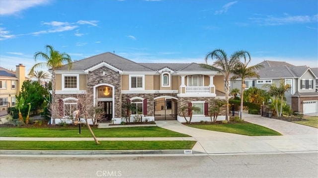 view of front of home featuring stucco siding, a balcony, concrete driveway, and a front yard