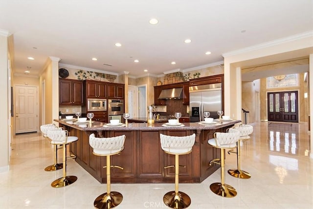 kitchen with a spacious island, backsplash, extractor fan, built in appliances, and a breakfast bar