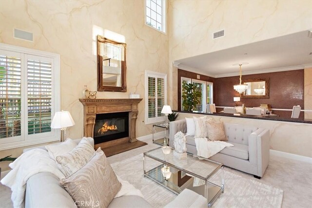 living room with a glass covered fireplace, crown molding, visible vents, and a chandelier