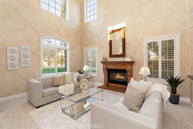 living area with a glass covered fireplace, baseboards, a towering ceiling, and carpet floors