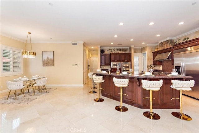 kitchen with a kitchen bar, built in appliances, crown molding, and baseboards