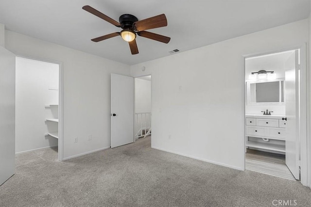 unfurnished bedroom with connected bathroom, sink, a walk in closet, ceiling fan, and light carpet