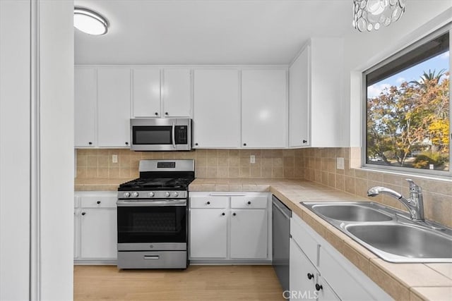 kitchen featuring sink, white cabinetry, stainless steel appliances, tasteful backsplash, and tile counters