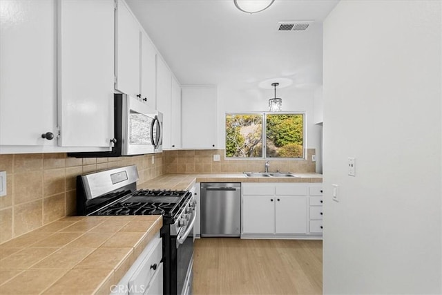 kitchen featuring sink, hanging light fixtures, stainless steel appliances, white cabinets, and tile countertops