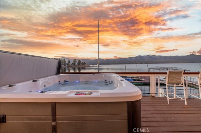 deck at dusk featuring a water and mountain view and a hot tub