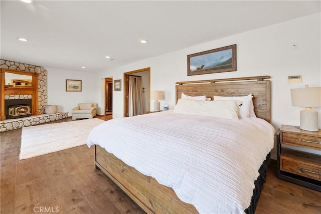 bedroom with a stone fireplace and dark hardwood / wood-style floors