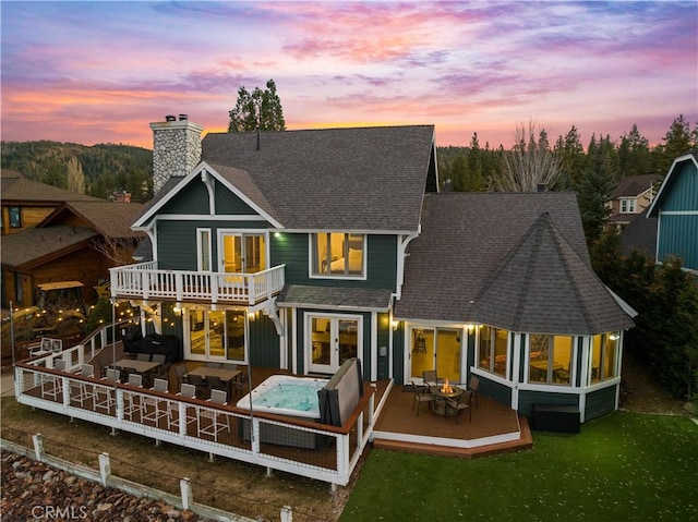 back house at dusk with a yard, french doors, a balcony, a sunroom, and a deck