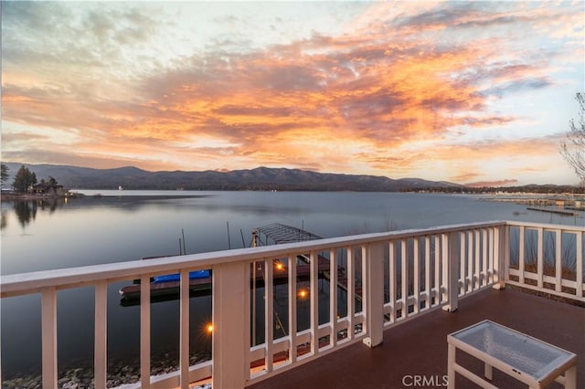 balcony at dusk featuring a water and mountain view