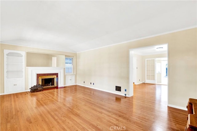 unfurnished living room featuring built in shelves, a fireplace, crown molding, and hardwood / wood-style floors