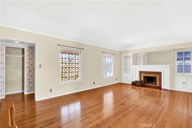 unfurnished living room featuring wood-type flooring, built in features, crown molding, and a brick fireplace