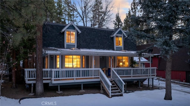 snow covered back of property featuring covered porch