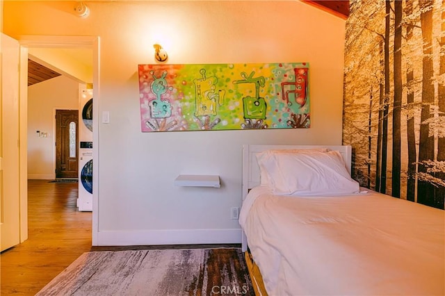 bedroom featuring stacked washing maching and dryer, wooden ceiling, hardwood / wood-style floors, and lofted ceiling with beams