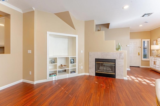 unfurnished living room featuring built in features, crown molding, a fireplace, and hardwood / wood-style flooring