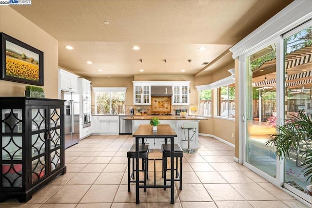 kitchen with appliances with stainless steel finishes, a breakfast bar, a kitchen island, white cabinets, and light tile patterned flooring