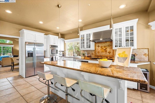 kitchen with a kitchen breakfast bar, appliances with stainless steel finishes, hanging light fixtures, stone counters, and wall chimney range hood