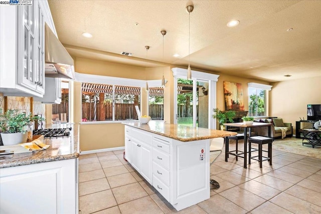 kitchen with light stone counters, pendant lighting, a kitchen island, white cabinetry, and a kitchen breakfast bar