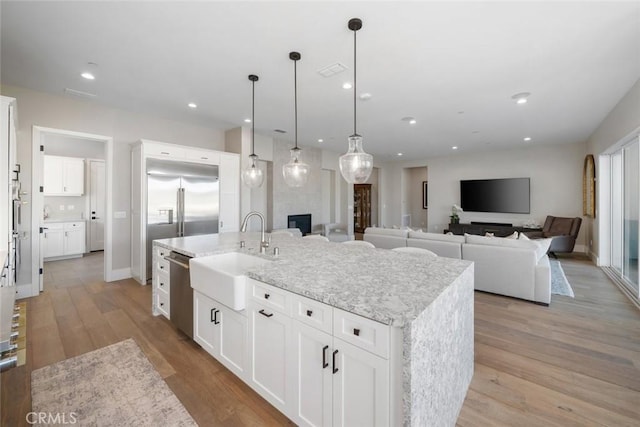 kitchen with hanging light fixtures, an island with sink, stainless steel appliances, white cabinetry, and sink