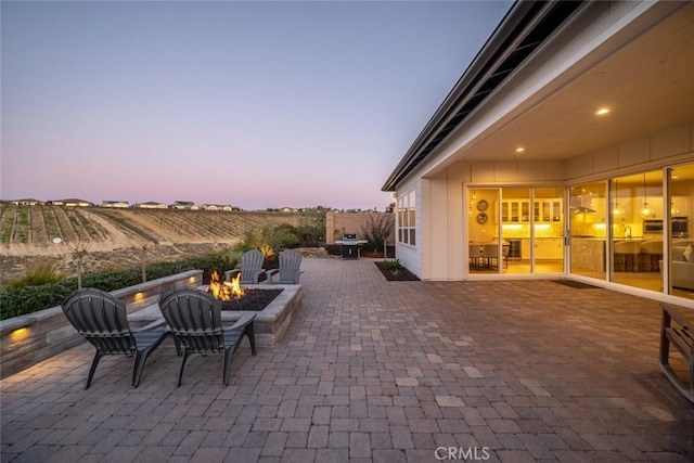 patio terrace at dusk featuring a fire pit and grilling area