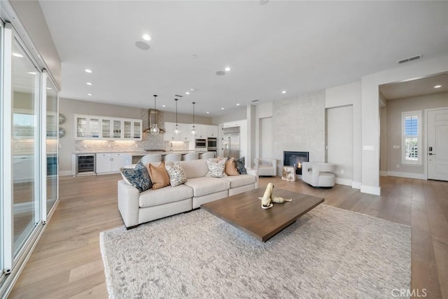 living room with a large fireplace, beverage cooler, and light wood-type flooring