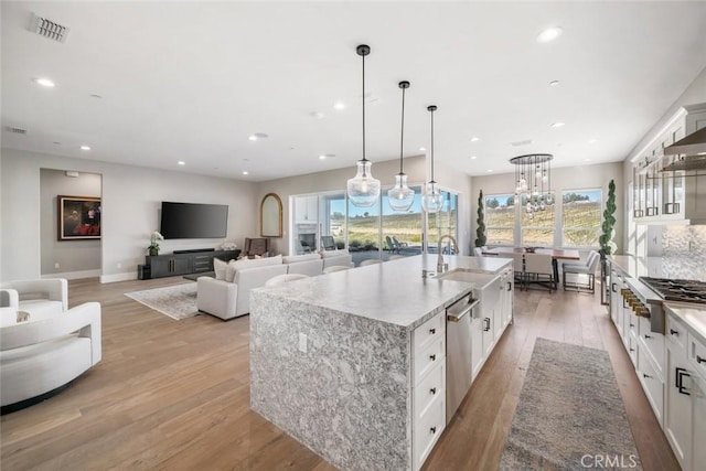 kitchen featuring decorative light fixtures, stainless steel appliances, a large island with sink, white cabinets, and sink