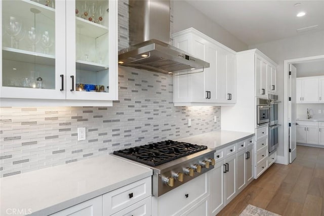 kitchen featuring dark wood-type flooring, wall chimney exhaust hood, decorative backsplash, stainless steel gas stovetop, and white cabinets