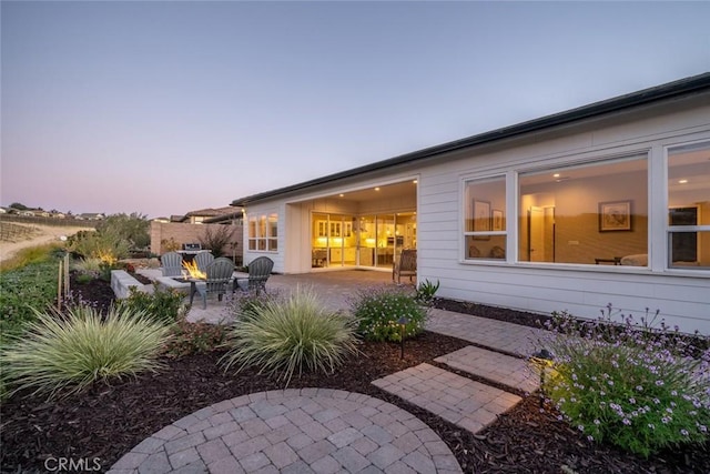 back house at dusk featuring an outdoor fire pit and a patio