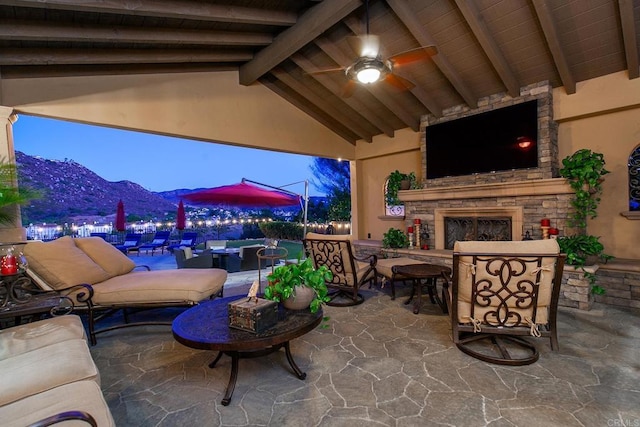 patio terrace at dusk featuring ceiling fan and an outdoor stone fireplace