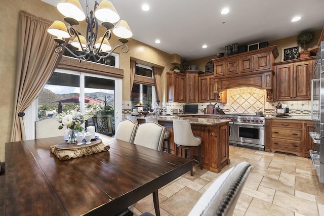 kitchen with light stone counters, range with two ovens, pendant lighting, a center island, and an inviting chandelier