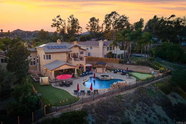 pool at dusk with a patio and an in ground hot tub