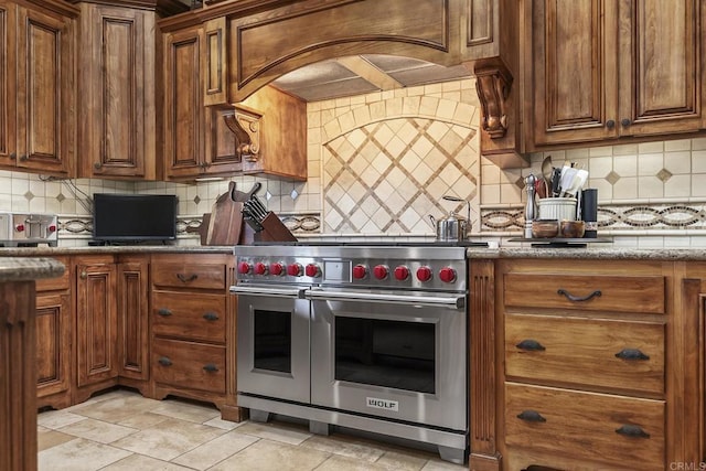 kitchen featuring custom exhaust hood, light tile patterned flooring, tasteful backsplash, and range with two ovens