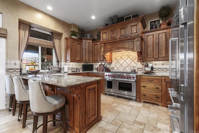 kitchen with high end appliances, a breakfast bar, decorative backsplash, dark stone countertops, and sink