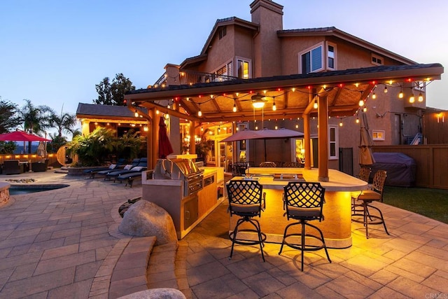 patio terrace at dusk featuring exterior bar, area for grilling, exterior kitchen, and a gazebo