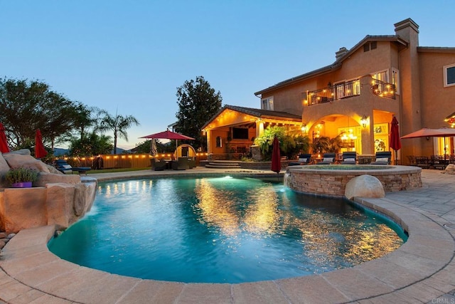 pool at dusk with a patio and pool water feature