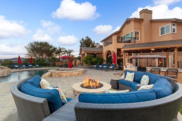 view of patio with a balcony, an outdoor living space with a fire pit, and a pool with connected hot tub