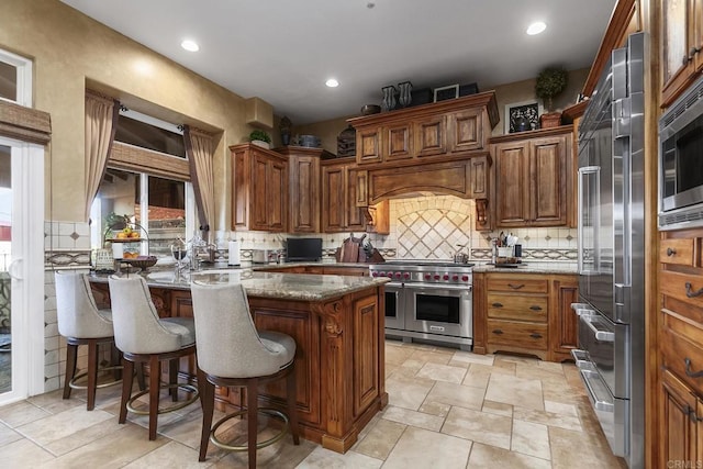 kitchen featuring backsplash, built in appliances, a peninsula, a kitchen breakfast bar, and stone countertops